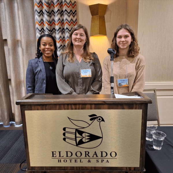 Three women smiling in front of a desk with a gold plaque reading "El Dorado Hotel & Spa".