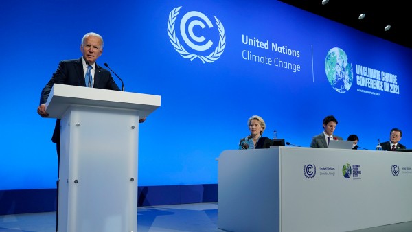 Joe Biden speaking at a podium, with other world leaders seated next to him, in front of a blue screen that reads United Nations Climate Change