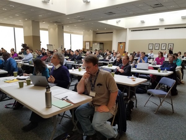 Photo of the meeting room with several attentive attendees.